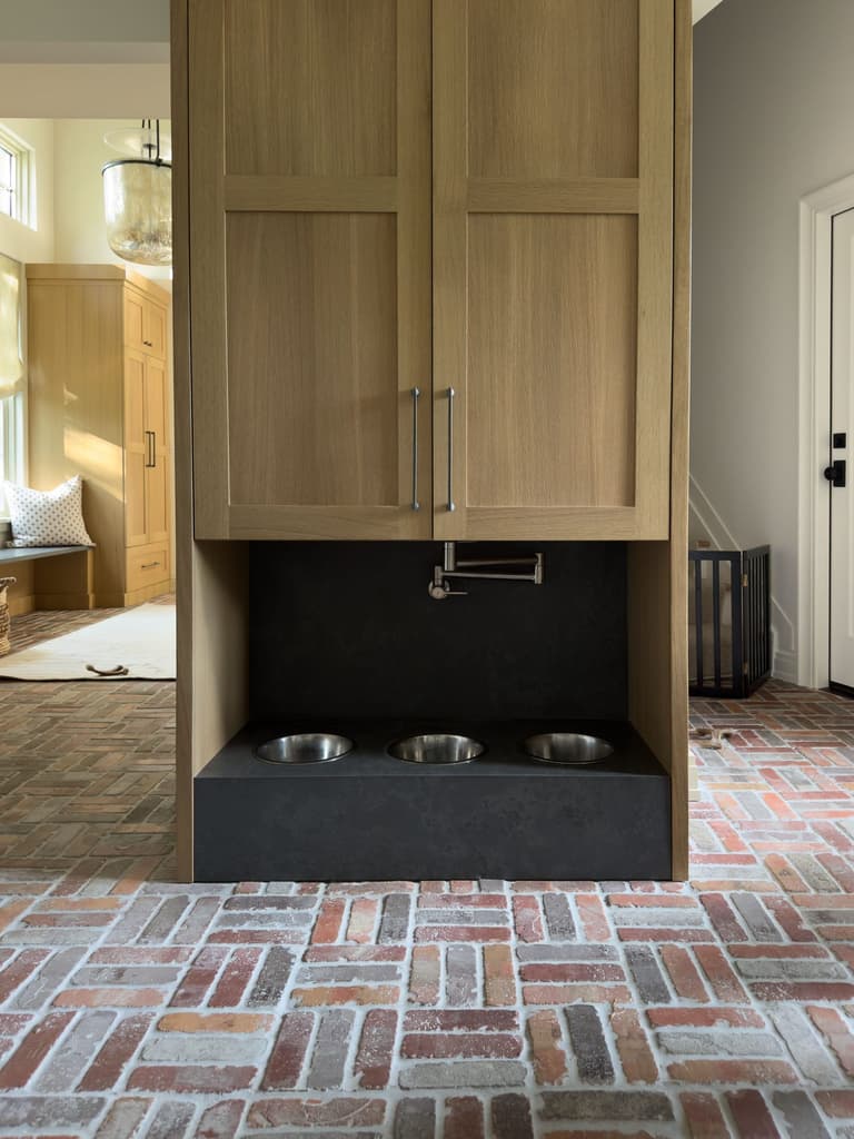 White oak mudroom cabinetry above a soapstone feeding station with a pot filler, on a herringbone brick floor in a Mendham, NJ renovation by Michael Robert Construction