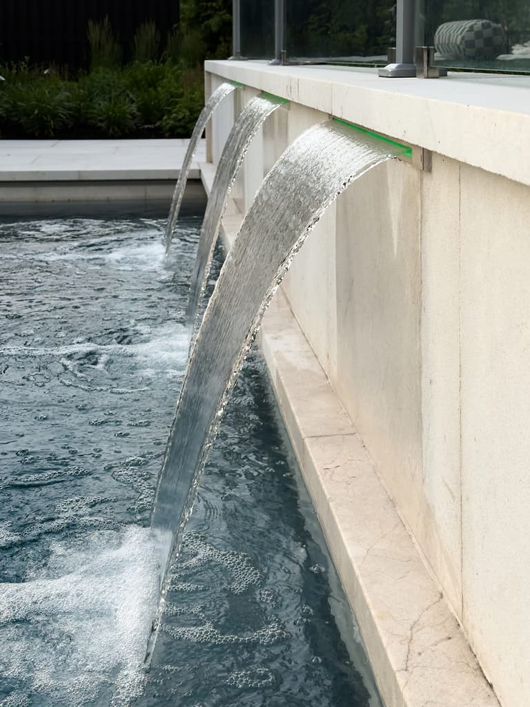 Water sheeting from a limestone spillway into the pool of a Westfield, NJ outdoor living project by Michael Robert Construction