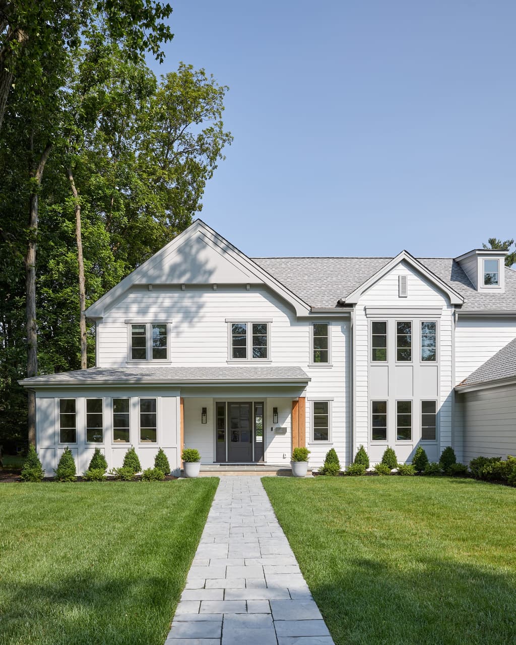 Front portico with cedar accents on a white Westfield, NJ home, approached by a paver walkway between clipped boxwood, built by Michael Robert Construction