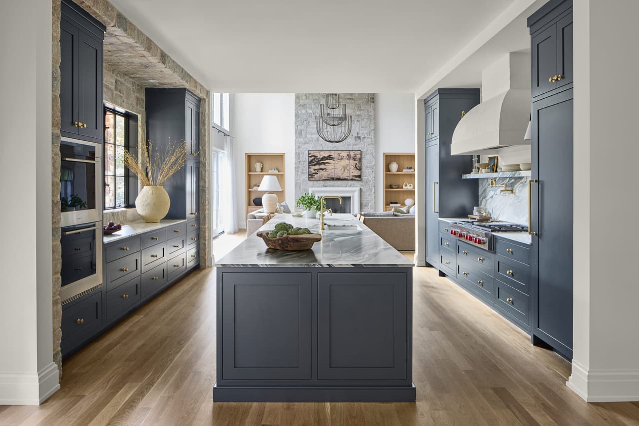 Marble-topped island and navy cabinetry in a whole-home renovation kitchen opening to a stone fireplace in Mendham, NJ, by Michael Robert Construction